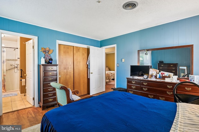 bedroom with a textured ceiling, ensuite bathroom, a closet, and wood-type flooring