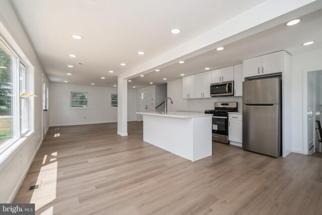 kitchen featuring appliances with stainless steel finishes, light hardwood / wood-style flooring, a wealth of natural light, and white cabinetry