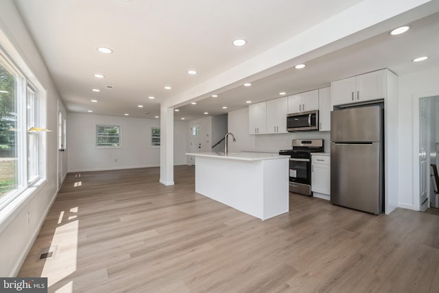 kitchen featuring light wood-type flooring, appliances with stainless steel finishes, white cabinetry, and a kitchen island with sink