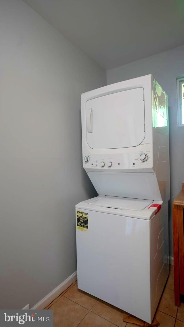 laundry area with stacked washer / drying machine and light tile patterned floors