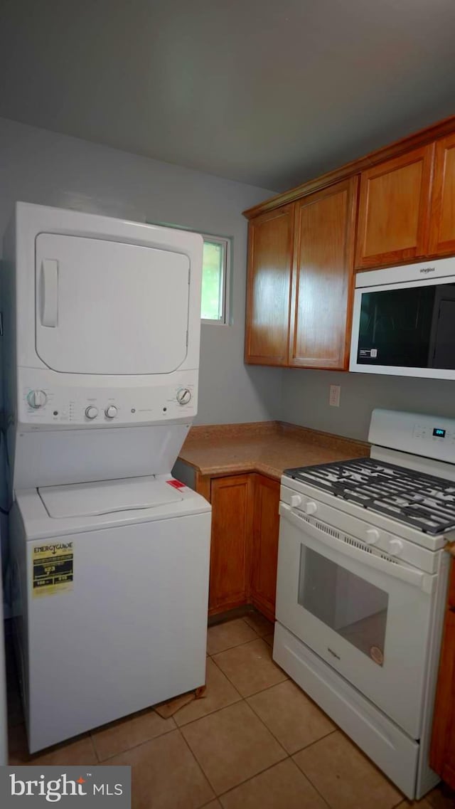 kitchen with white gas range, stacked washer / drying machine, and light tile patterned flooring