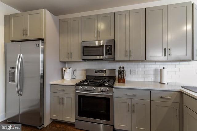 kitchen featuring appliances with stainless steel finishes, gray cabinetry, decorative backsplash, and light stone counters