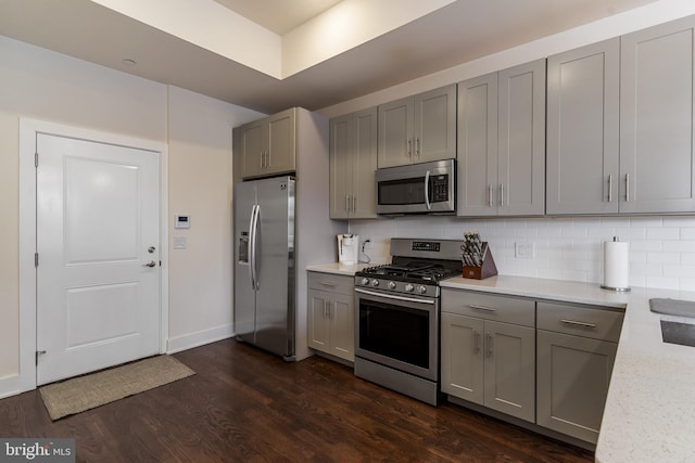 kitchen with dark wood-type flooring, stainless steel appliances, decorative backsplash, and gray cabinets