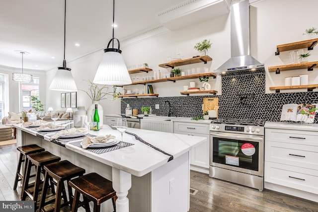 kitchen with pendant lighting, dark hardwood / wood-style floors, white cabinets, stainless steel gas range oven, and wall chimney range hood