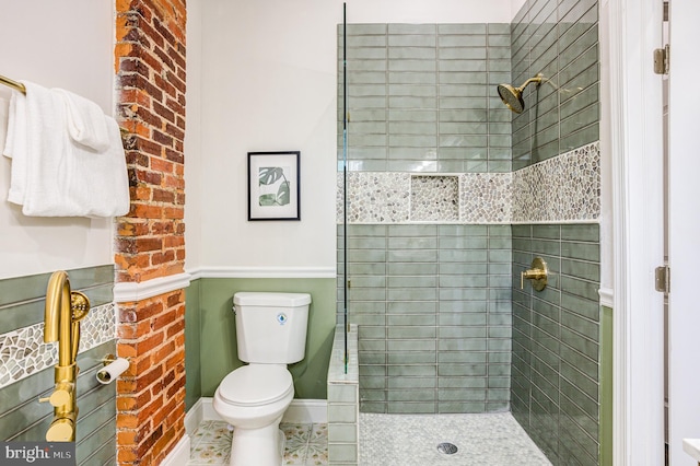 bathroom with a tile shower, tile patterned flooring, toilet, and brick wall