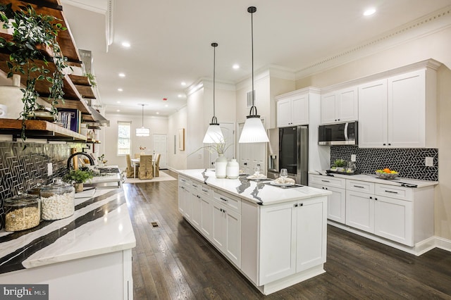 kitchen with appliances with stainless steel finishes, white cabinetry, dark hardwood / wood-style flooring, pendant lighting, and a center island with sink