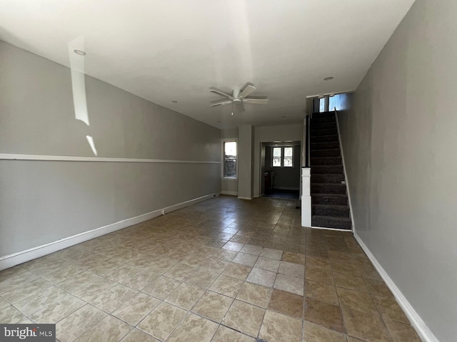 interior space with baseboards, ceiling fan, and stairs