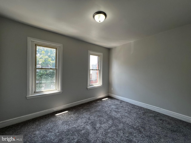 unfurnished room with dark carpet and baseboards