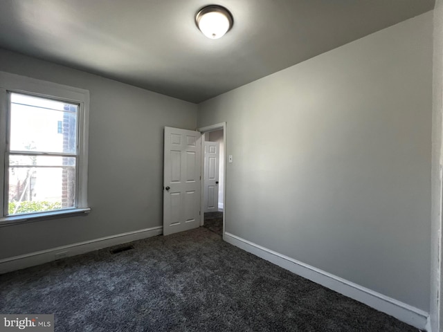 unfurnished room with baseboards, visible vents, and dark colored carpet