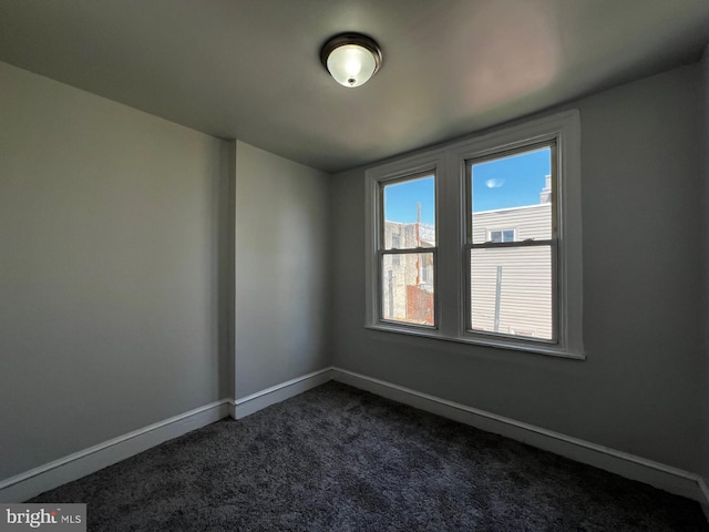 spare room with baseboards and dark carpet