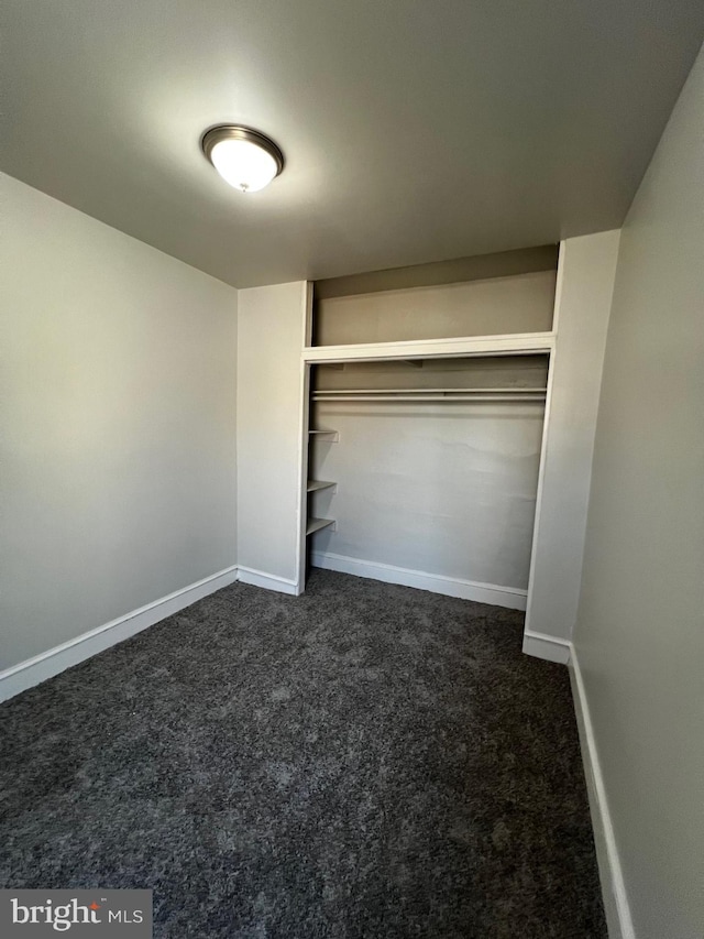 unfurnished bedroom with a closet, baseboards, and dark carpet