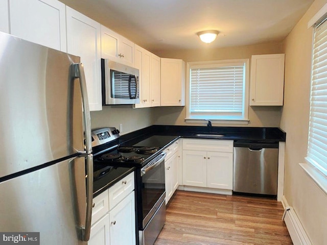 kitchen with sink, light hardwood / wood-style flooring, appliances with stainless steel finishes, white cabinets, and a baseboard radiator