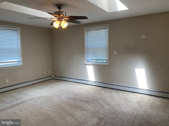 carpeted empty room with ceiling fan, a skylight, and a baseboard heating unit