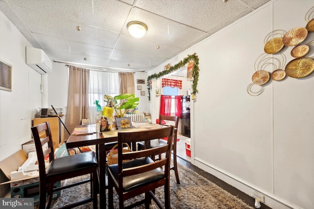 dining space with a wall mounted air conditioner, wood-type flooring, and a paneled ceiling