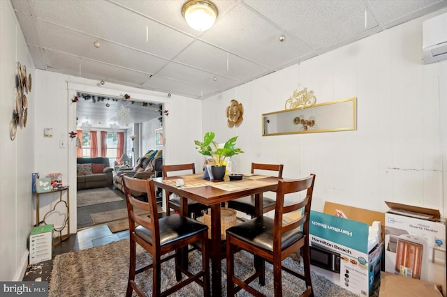 dining room with tile patterned floors, a wall unit AC, and a paneled ceiling