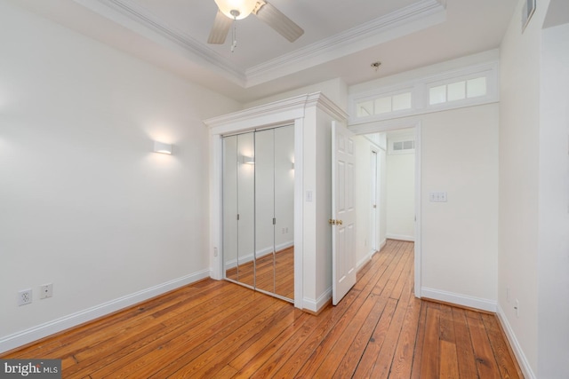 unfurnished bedroom with hardwood / wood-style flooring, crown molding, a closet, a tray ceiling, and ceiling fan