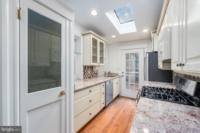 kitchen with light stone counters, light wood-type flooring, appliances with stainless steel finishes, and a skylight