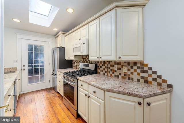 kitchen with a skylight, appliances with stainless steel finishes, light stone countertops, light hardwood / wood-style floors, and tasteful backsplash