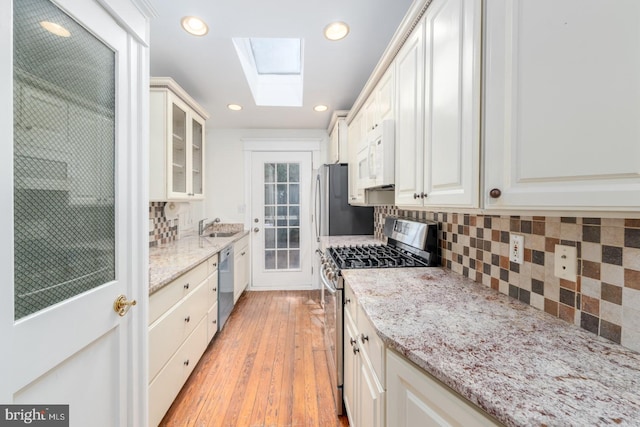 kitchen with light hardwood / wood-style flooring, appliances with stainless steel finishes, white cabinetry, and a skylight