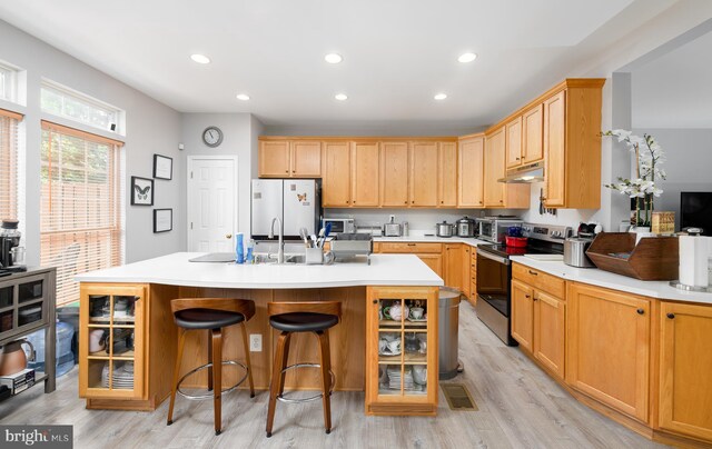 kitchen with stainless steel range with electric cooktop, a kitchen island with sink, light wood-type flooring, white refrigerator, and a breakfast bar