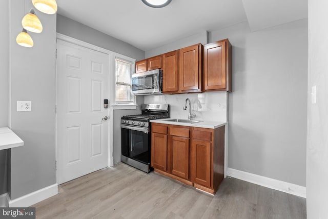 kitchen with sink, appliances with stainless steel finishes, decorative light fixtures, and light wood-type flooring