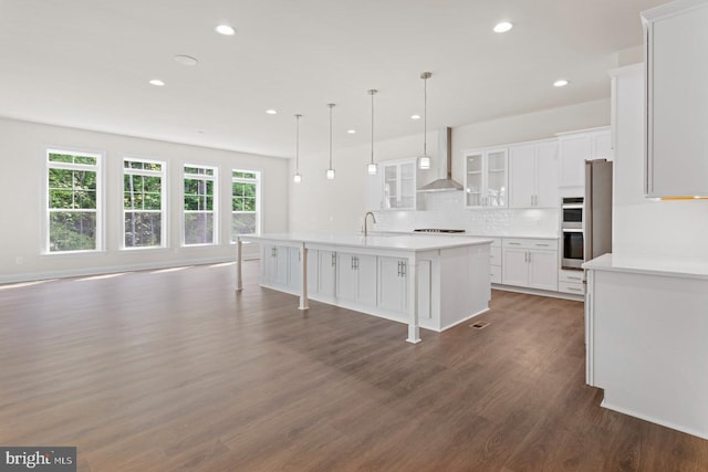 kitchen featuring wall chimney range hood, dark hardwood / wood-style floors, a healthy amount of sunlight, and a center island with sink