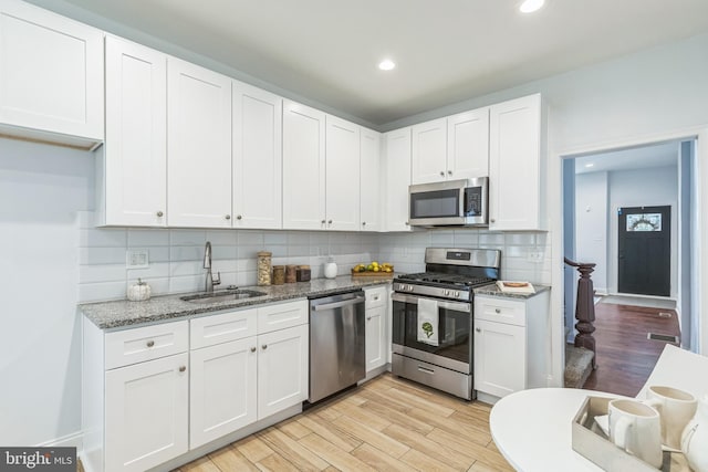 kitchen with sink, stainless steel appliances, light hardwood / wood-style floors, light stone countertops, and white cabinets