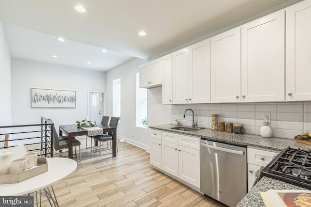 kitchen with white cabinetry, dark stone counters, dishwasher, and sink