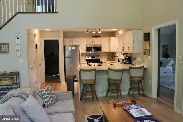 living room with a towering ceiling, sink, and light wood-type flooring