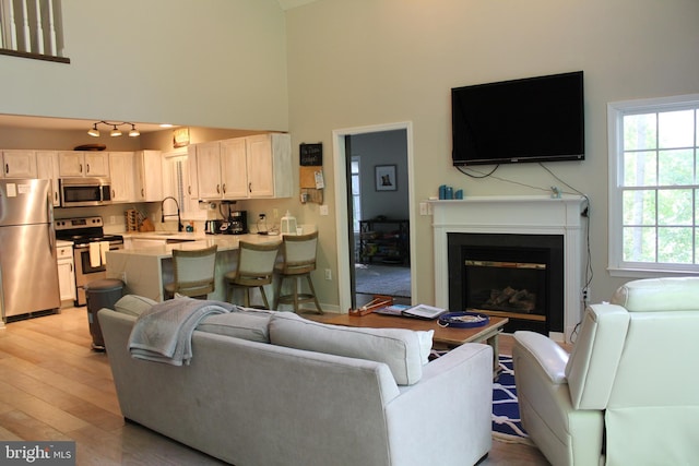 living room featuring a high ceiling, light wood-type flooring, and sink