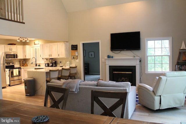 living room with high vaulted ceiling, sink, and light hardwood / wood-style floors