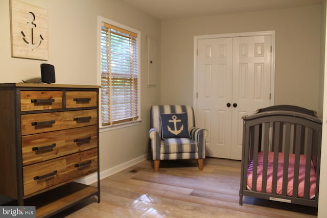 bedroom with a nursery area, light wood-type flooring, and a closet