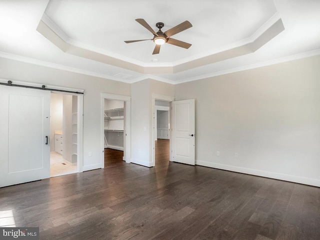 unfurnished bedroom with a spacious closet, a closet, a raised ceiling, ceiling fan, and a barn door