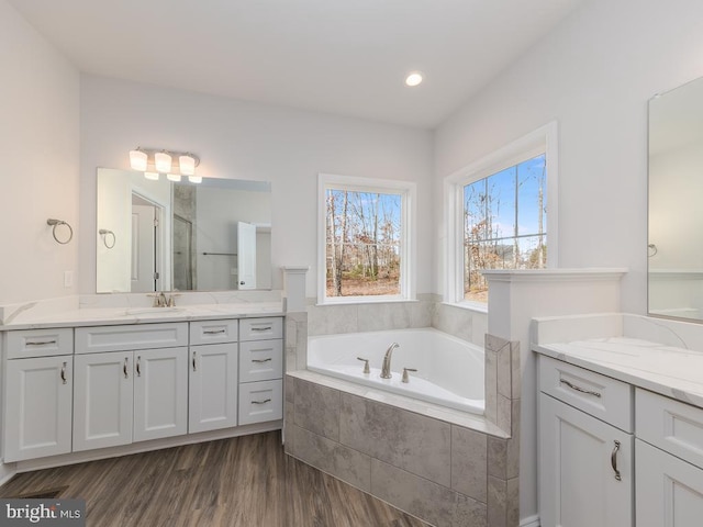 bathroom with tiled bath, vanity, and wood-type flooring