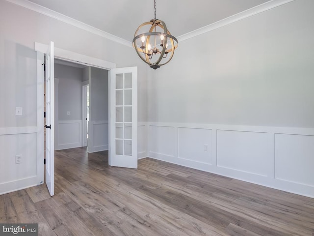 empty room with hardwood / wood-style flooring, french doors, ornamental molding, and a notable chandelier