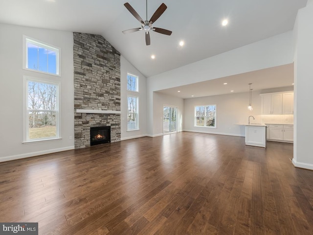 unfurnished living room with dark hardwood / wood-style flooring, a stone fireplace, sink, high vaulted ceiling, and ceiling fan