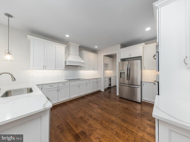 kitchen with white cabinets, stainless steel refrigerator with ice dispenser, premium range hood, sink, and light stone counters