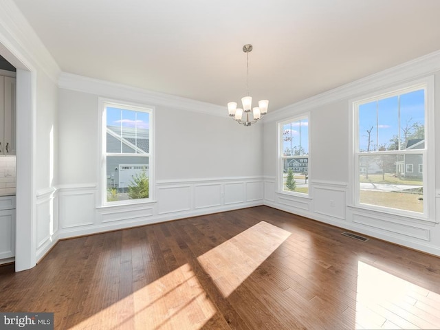 unfurnished dining area featuring dark wood-type flooring, crown molding, and a notable chandelier