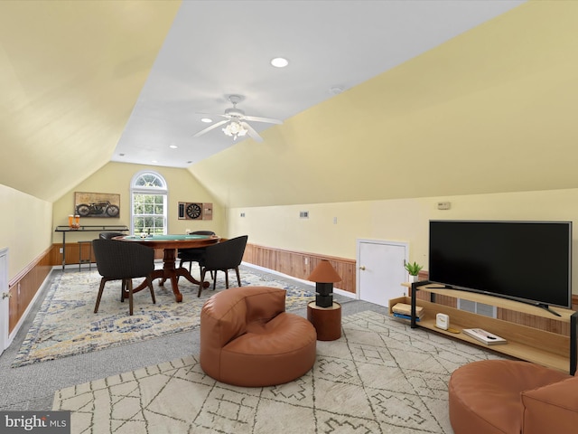 carpeted living room featuring ceiling fan, vaulted ceiling, and wooden walls