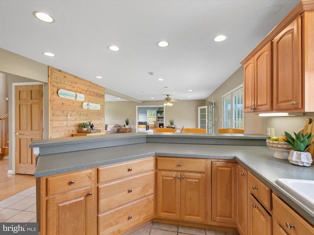 kitchen featuring wood walls, ceiling fan, light tile patterned floors, and kitchen peninsula