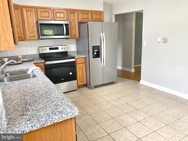 kitchen featuring stainless steel appliances, sink, backsplash, light tile patterned flooring, and light stone counters