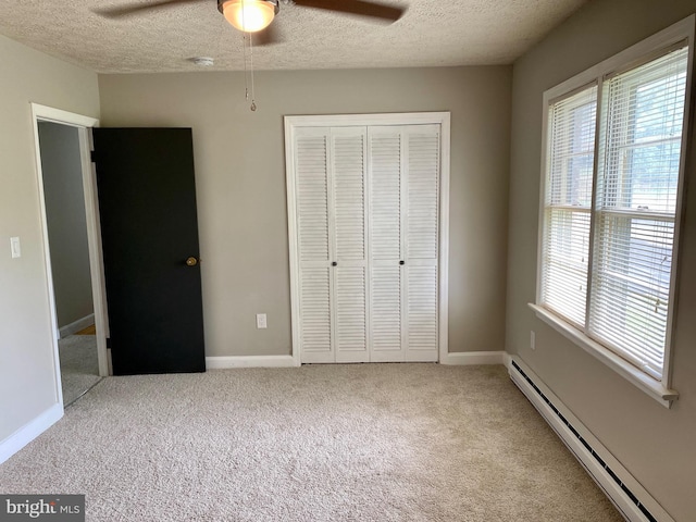 unfurnished bedroom featuring baseboard heating, a textured ceiling, carpet floors, a closet, and ceiling fan