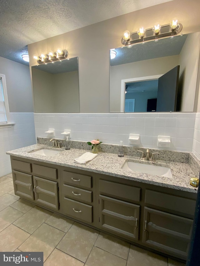 bathroom featuring a textured ceiling, tile patterned floors, vanity, and tile walls