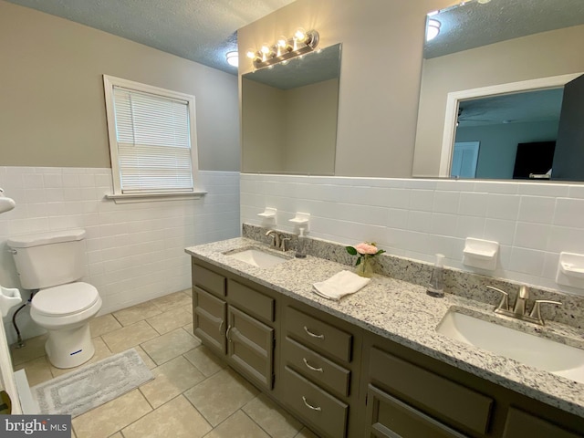 bathroom featuring toilet, vanity, tile walls, tile patterned floors, and a textured ceiling