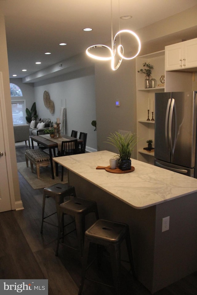 kitchen featuring stainless steel refrigerator, decorative light fixtures, a breakfast bar, dark hardwood / wood-style floors, and white cabinets