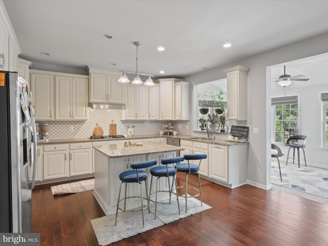 kitchen featuring sink, appliances with stainless steel finishes, hanging light fixtures, light stone counters, and a kitchen island