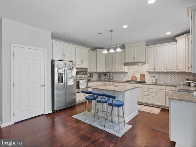 kitchen featuring hanging light fixtures, a kitchen island, stainless steel appliances, light stone counters, and a kitchen bar