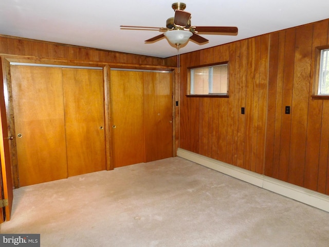 unfurnished bedroom featuring wood walls, a baseboard radiator, carpet floors, and ceiling fan