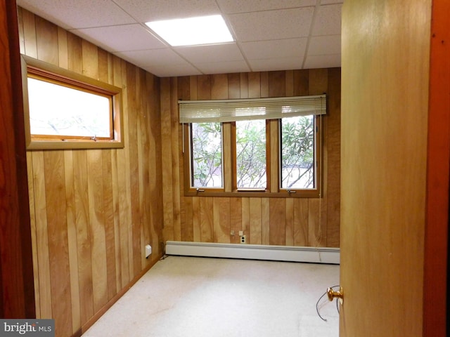 carpeted empty room featuring a baseboard heating unit and a drop ceiling