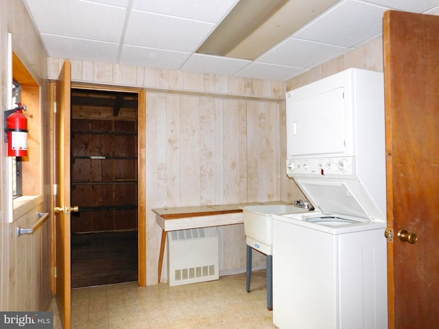 clothes washing area with stacked washer / dryer, radiator, light tile patterned floors, and wooden walls